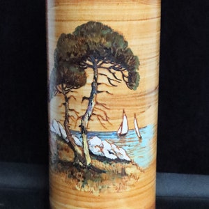 May include: A ceramic vase with a wood-grain pattern and a painted scene of a pine tree by a body of water with sailboats. The vase is brown with blue, green, and white accents.