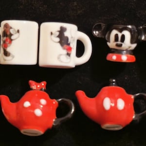 Puede incluir: Colección de tazas, teteras y tazas de cerámica en miniatura con temática de Disney. Las tazas son blancas con diseños de Mickey Mouse negro y lazos de Minnie Mouse. Las teteras son rojas con lunares blancos y diseños de Mickey.