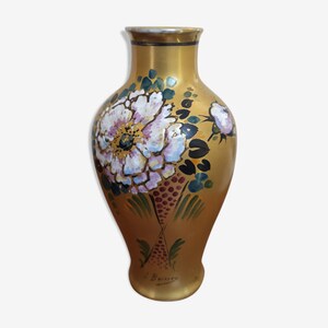 Op de afbeelding: Een gouden keramische vaas met een bloemenmotief. De vaas is versierd met roze, witte en groene bloemen. De vaas is onderaan gesigneerd met "J. Bouvier".