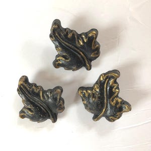 May include: Three decorative leaf-shaped cabinet knobs. The knobs are black with gold accents, featuring detailed veining and a textured finish. These hardware pieces are ideal for adding a touch of nature-inspired elegance to furniture or cabinetry.