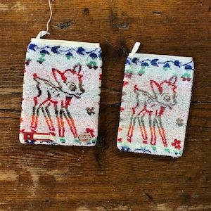 May include: Two rectangular white washcloths with a Bambi design. The washcloths have a white background with a colorful border and a Bambi illustration in the center. The Bambi illustration is in shades of brown, red, and orange.