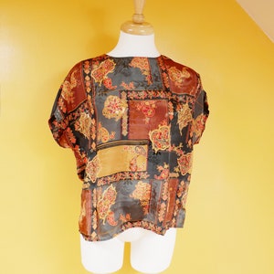 Peut inclure: Un chemisier à motifs avec un design patchwork dans des tons de brun, or, rouge et noir. Le chemisier est fait d'un tissu transparent et a une coupe ample.