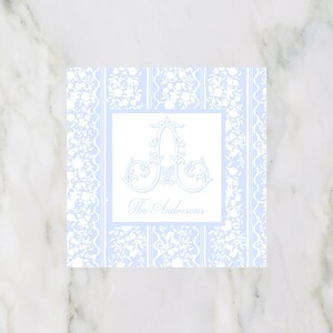 May include: Square, light blue and white monogram card with a floral design. The card features a large, ornate letter "A" in the center, with the name "The Andersons" below. The background has a delicate, repeating pattern.