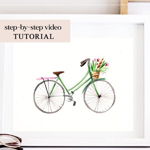 Könnte beinhalten: Ein Aquarellbild eines grünen Fahrrads mit einem Blumenkorb am Lenker. Das Fahrrad hat einen rosa Sattel und weiße Reifen. Das Bild ist in einem weißen Rahmen gerahmt.