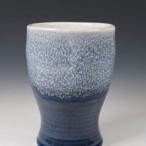 May include: A ceramic drinking glass with a white and blue glaze. The top of the glass is white with a speckled blue glaze. The bottom of the glass is a solid blue glaze.