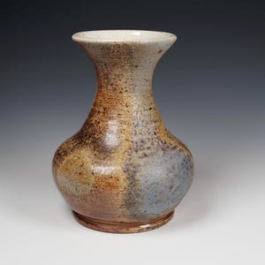 May include: A handcrafted ceramic vase with a bulbous body and a flared neck. The vase features a blend of earthy tones, including brown, tan, and gray, with a textured surface. The base has a circular design. A decorative piece for the home.