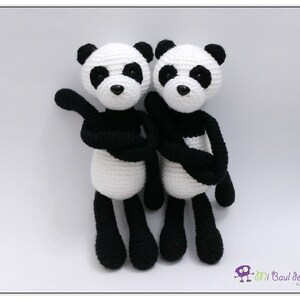 May include: Two crocheted panda bears, one black and white and the other white and black, are standing side by side. They are both wearing black crocheted scarves.
