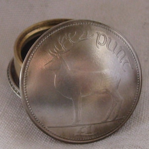 May include: A small round metal container featuring a lid made from a silver-coloured coin. The coin lid displays an embossed image of a deer and the text "punt" along the edge. The base of the container is made of a contrasting brass-coloured metal.