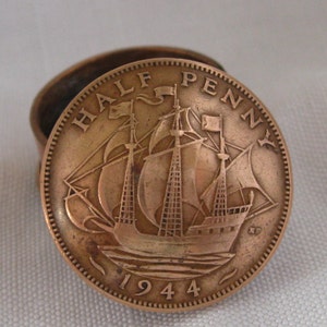Puede incluir: Una moneda de media penique de cobre de 1944, con un diseño de velero. La moneda está colocada en un pequeño recipiente redondo de cobre. Los detalles de la moneda incluyen las palabras "HALF PENNY" y el año "1944".