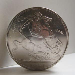 May include: A silver coin featuring a detailed relief of a knight on horseback slaying a dragon. The coin has a textured edge and the year 1951 is visible at the bottom. The coin is round and has a shiny, reflective surface.