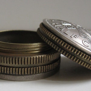 Puede incluir: Primer plano de dos monedas antiguas, una parcialmente abierta, que revela un interior de latón. Las monedas tienen una combinación de colores plateado y dorado con patrones de borde detallados. Una moneda muestra el texto "HALF CROWN".