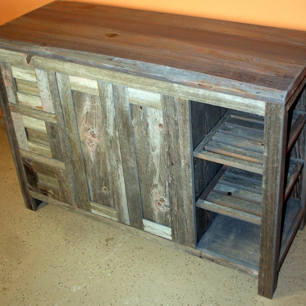 May include: A rustic wooden cabinet with a distressed gray finish. The cabinet has a single door with a unique patchwork design and open shelves on the right side. The top is made of a single piece of wood with a natural wood grain.