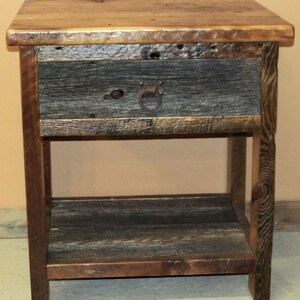 May include: A rustic wooden nightstand with a single drawer and a lower shelf. The drawer has a metal ring pull and the wood has a natural, weathered finish.