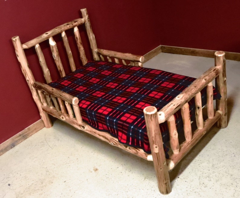May include: A wooden toddler bed with a red and black plaid blanket. The bed is made of natural wood with a rustic finish.