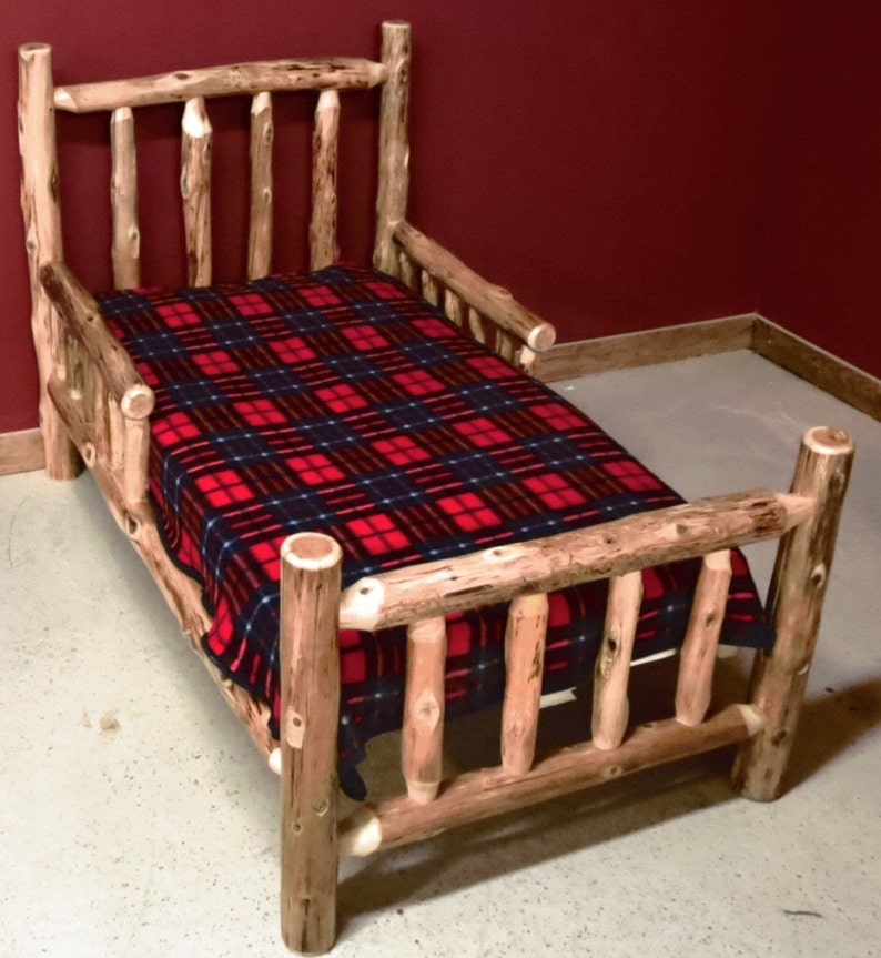 May include: A wooden toddler bed with a red and black plaid blanket. The bed has a high headboard and footboard with a safety rail on one side.