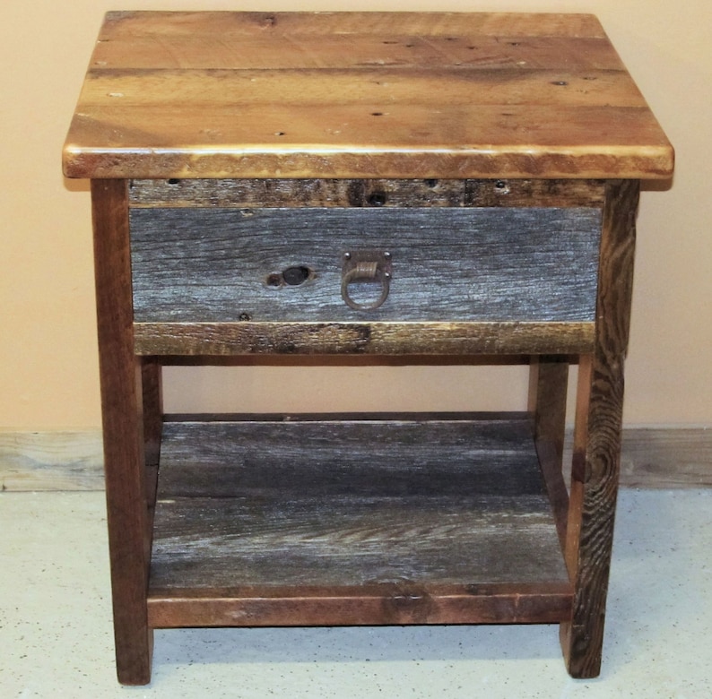 May include: A rustic wooden end table with a single drawer and a lower shelf. The table is made of reclaimed wood with a natural finish. The drawer has a metal ring pull.