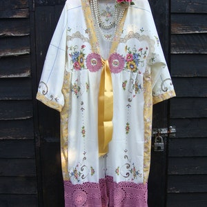 May include: A white vintage-style dress with floral embroidery and lace trim. The dress has a yellow ribbon tied at the waist and a pearl necklace.