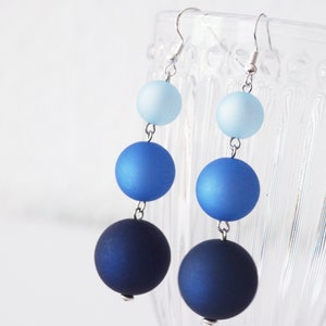 May include: A pair of dangle earrings with three graduated blue glass beads. The beads are a light blue, a medium blue, and a dark blue. The earrings are silver.