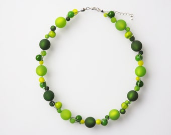 May include: A multi-strand necklace featuring an assortment of round beads in various shades of green, including lime, forest, and olive. The beads have matte and glossy finishes and are strung on thin silver-toned wire with a metal lobster clasp.