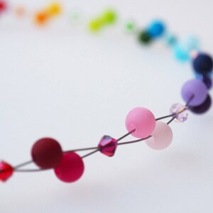 May include: A close-up of a colorful beaded necklace with pink, red, and purple beads. The beads are strung on a wire and are separated by small crystal beads.
