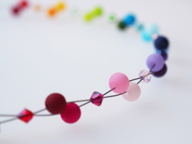 May include: A close-up of a colorful beaded necklace with pink, red, and purple beads. The beads are strung on a wire and are separated by small crystal beads.
