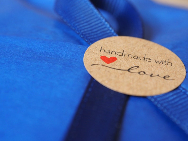 May include: A brown paper circle tag with the text "handmade with love" in black lettering and a red heart. The tag is tied to a blue ribbon.