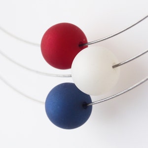 May include: A necklace with three round beads in red, white, and blue colors. The beads are strung on a silver wire.