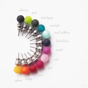 Op de afbeelding: Een set van 14 kleurrijke ronde kastknoppen met zilveren bases. De knoppen zijn in een halve cirkel gerangschikt en gelabeld met hun bijbehorende kleuren in het Duits.