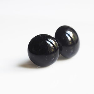 May include: A pair of black stud earrings. The earrings are round and have a smooth, glossy finish.