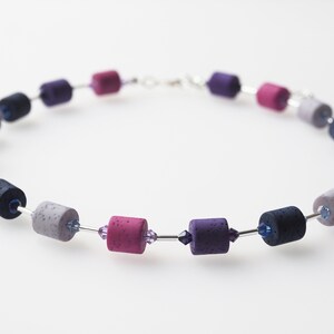 May include: A necklace made of purple, pink and grey cylindrical beads with silver wire and small crystal accents.