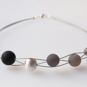 May include: A silver and black necklace with a silver bead and five black and grey beads.