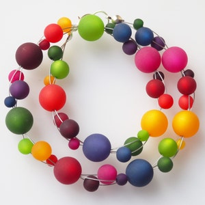 May include: A rainbow colored necklace made of glass beads strung on silver wire. The beads are various sizes and shapes, and the necklace is a statement piece.