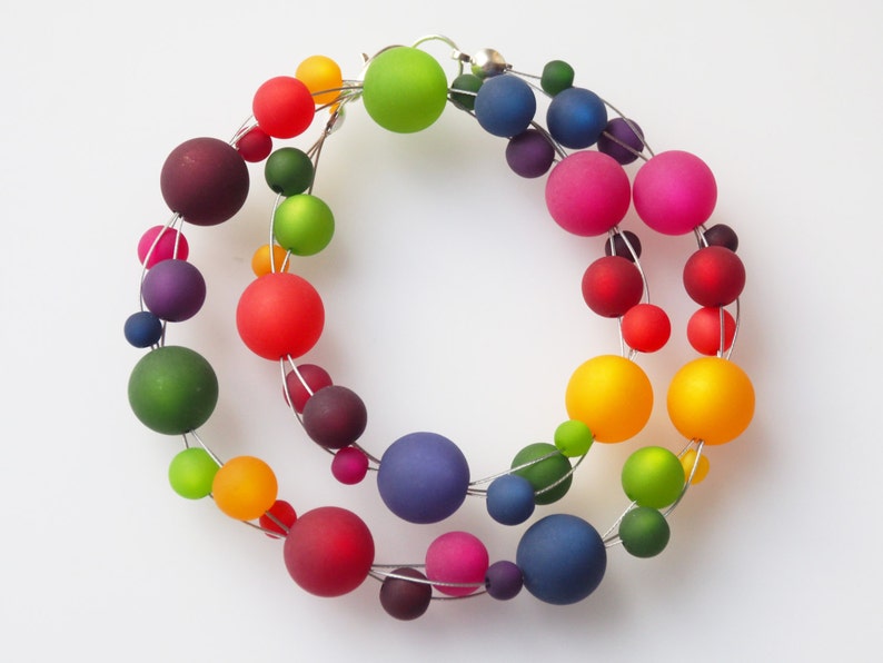 May include: A rainbow colored necklace made of glass beads strung on silver wire. The beads are various sizes and shapes, and the necklace is a statement piece.