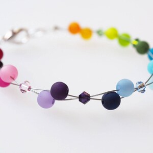 May include: A rainbow colored beaded bracelet with a silver clasp. The beads are made of glass and are in shades of red, orange, yellow, green, blue, indigo, and violet.
