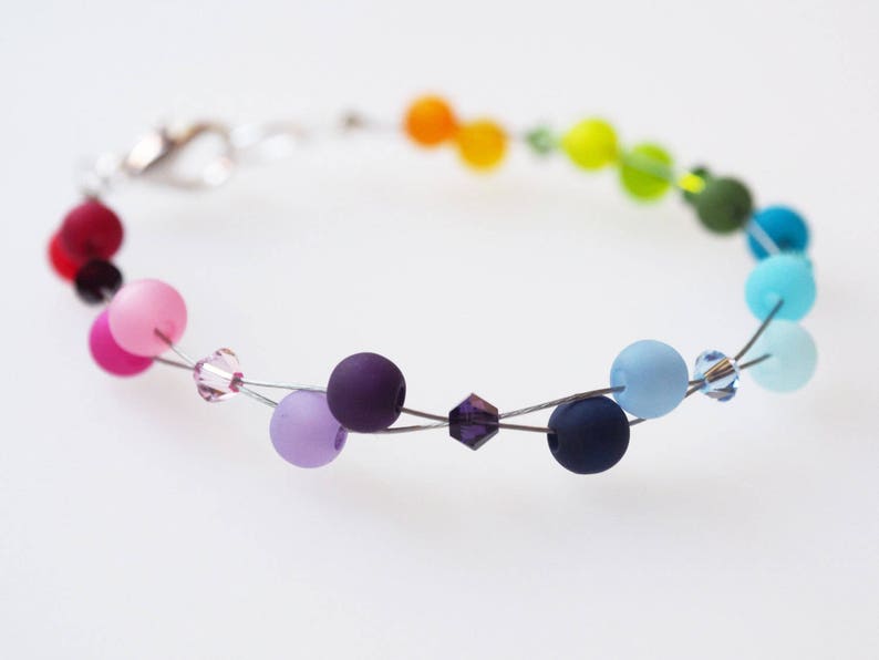 May include: A rainbow colored beaded bracelet with a silver clasp. The beads are made of glass and are in shades of red, orange, yellow, green, blue, indigo, and violet.