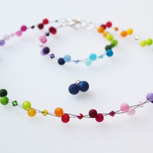 May include: A rainbow colored beaded necklace with matching earrings. The necklace is made of small, round beads strung on a thin wire. The beads are in a rainbow order, starting with red and ending with purple. The earrings are also made of small, round beads in the same rainbow order.