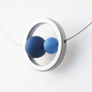 May include: A silver necklace with a circle pendant and two blue beads. The beads are different shades of blue.