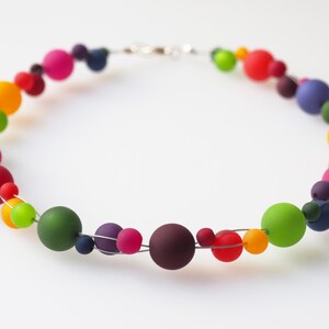 May include: A colorful necklace made of round beads in various shades of red, orange, yellow, green, blue, and purple. The beads are strung on a silver wire.