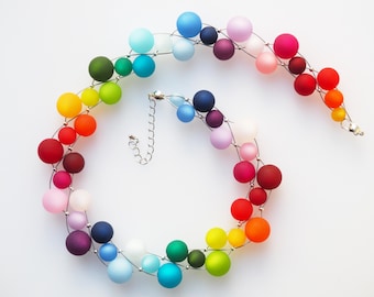 May include: A colorful necklace featuring a gradient of matte finish spheres in a rainbow of colors. The spheres are strung on a thin, silver-colored wire, with a silver clasp and extender chain. The necklace is displayed on a white background.