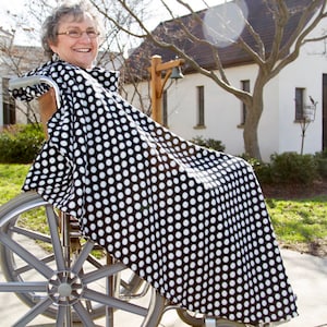 May include: A woman in a wheelchair is wearing a black and white polka dot wheelchair cover. The cover is made of a soft, comfortable fabric and is designed to keep the user warm and cozy.