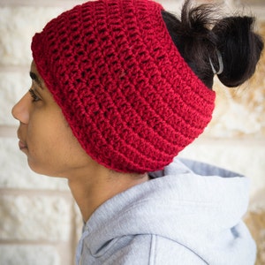 May include: A red crocheted headband with a hole in the back for a ponytail. The headband is worn by a person with a grey hoodie.