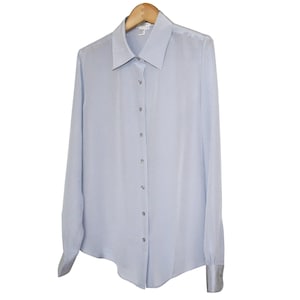 May include: A light blue long-sleeve button-down shirt with a classic collar and cuffs. The shirt is made of a smooth, possibly silk-like material and hangs on a wooden hanger. The shirt has a tailored fit and a subtle sheen.