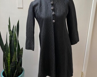May include: A black vintage dress with a geometric pattern and a row of decorative buttons down the front.