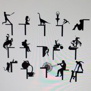 Puede incluir: Un conjunto de 12 figuras de jardín de metal en silueta negra. Las figuras incluyen un jugador de béisbol, una niña con una flor, un dinosaurio, una bailarina, una niña haciendo una voltereta, una mujer sentada, un vaquero montando un caballo, un hombre tocando la guitarra, un hombre montando una moto de cross, un nativo americano montando un caballo, un ratón, una mujer sirviendo té, un girasol, un hombre tocando la trompeta y un hombre ayudando a un niño a subir una escalera.