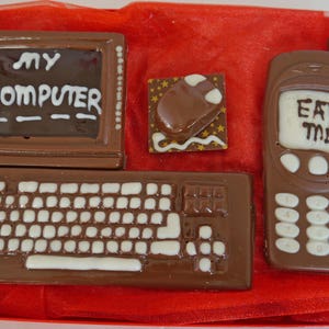 May include: A chocolate computer set with a monitor, keyboard, mouse, and a mobile phone that says "Eat Me".