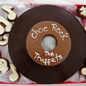 May include: A chocolate record shaped like a vinyl record with the words "Choc Rock The Truffets" written on it. The record is surrounded by white chocolate musical notes in a red box.