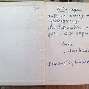 K&ouml;nnte beinhalten: Offenes Buch mit handschriftlichem deutschem Text in blauer Tinte. Der Text enth&auml;lt eine Widmung, ein Zitat und das Datum September 1964. Die Seiten des Buches sind cremefarben, und der Einband ist dunkelgr&uuml;n.