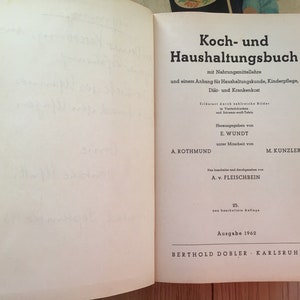 K&ouml;nnte beinhalten: Aufgeschlagenes Buch mit dem Titel "Koch- und Haushaltungsbuch" in deutscher Sprache. Der Einband zeigt schwarzen Text auf wei&szlig;em Hintergrund, einschlie&szlig;lich Titel, Untertitel und Autoreninformationen. Das Buch ist von 1962.