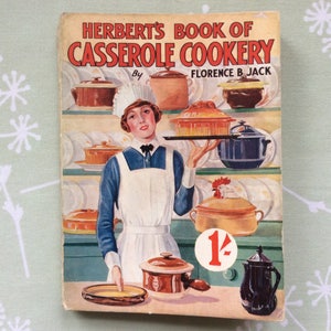 May include: Vintage cookbook cover titled "Herbert's Book of Casserole Cookery" by Florence B. Jack. The cover features an illustration of a woman in a white apron and cap, holding a tray of casseroles. Various casserole dishes are displayed on shelves in the background.