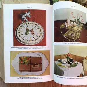 K&ouml;nnte beinhalten: Eine Seite aus einem Vintage-Kochbuch mit Illustrationen von Kuchen, einem Teeservice und einem Fr&uuml;hst&uuml;ckstisch. Die Seite enth&auml;lt deutschen Text und einen dekorativen Kuchen mit Marzipanmasken. Die Bilder sind farbenfroh und retro.